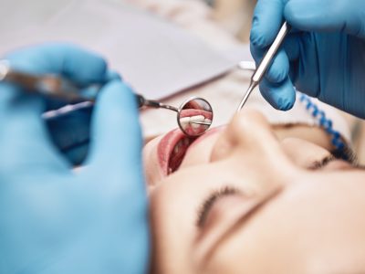 Close-up of woman opening her mouth wide during inspection of oral cavity. Dentist is checking up her teeth using dental tools. Medicine and health care concept. Focus on dental tools. Horizontal shot